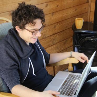 The writer, smiling, sits cross-legged in a chair, laptop on her lap.