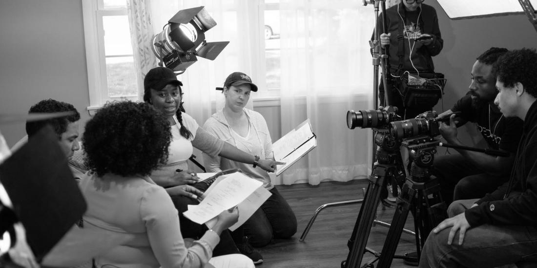 Director Alison Guessou talking with her cast in front of camera on set.