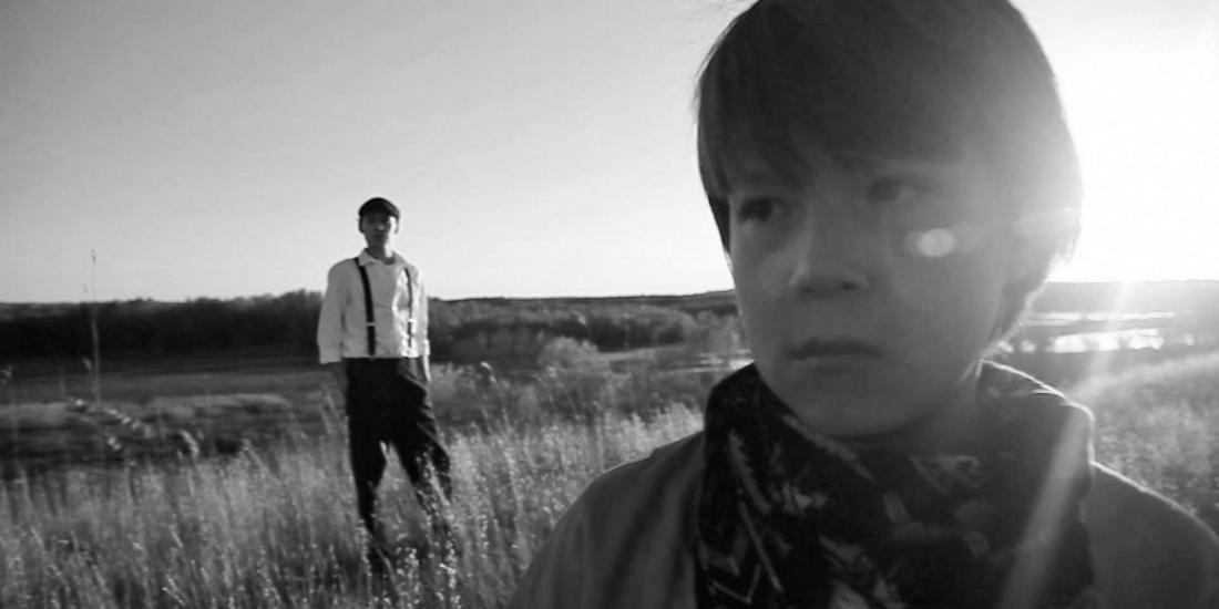 Black and white image of young person at the foreground and adult standing in a field.