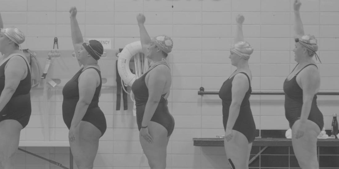 Group of synchronized swimmers outside of the pool raising their right fists.