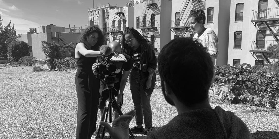 Filmmakers behind the camera interviewing a subject on a rooftop.