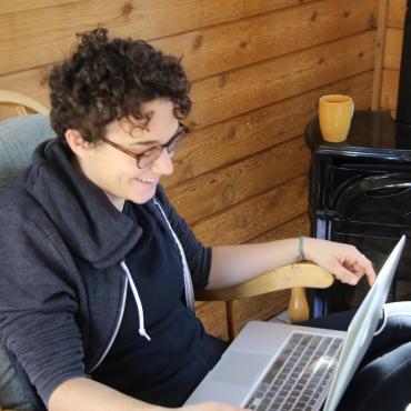 The writer, smiling, sits cross-legged in a chair, laptop on her lap.
