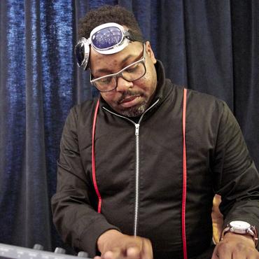 Dameun seated playing at his synthesizer rig.