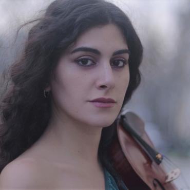Layale Chaker outside with her violin, smiling.