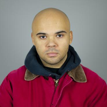 A man in red jacket stands on grey background and looks into camera.