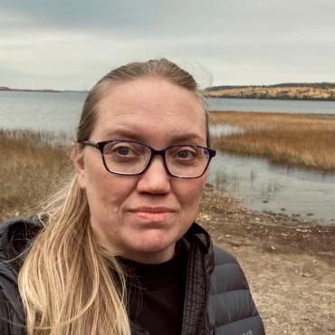 Catherine Meier, a forty-six year old visual artist, standing in front of Gunflint Lake looking slightly to the side of the camera.