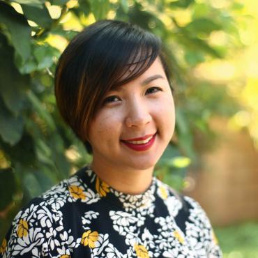 Writer Cathy Linh Che wearing a floral dress in front of her mother's lemon tree