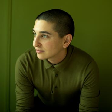 Headshot of a person in a green sweater in front of a green wall, looking to the side and not directly at the camera.