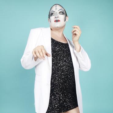 performer in short, black sequined dress and white dinner jacket wearing gender nonconforming makeup