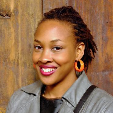 A photographer of writer Naomi Jackson smiling in front of a brown wall at Kara Walker's "A Subtlety" exhibition