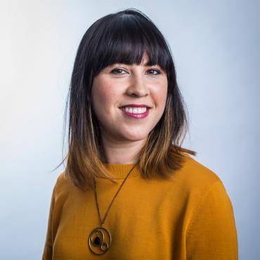 Portrait of Katie Gee Salisbury smiling and wearing a mustard yellow dress