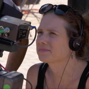 Kate Marks, a forty-something caucasian woman filmmaker staring into a monitor on set.