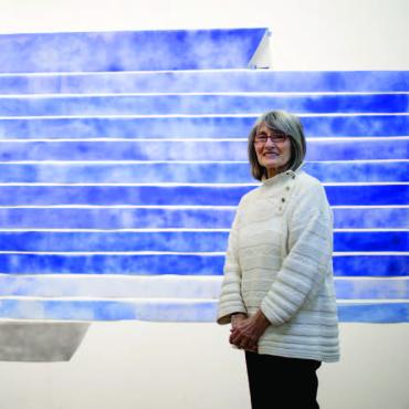 Women in a white sweater and black pants in front of an artwork with various shades of blue.