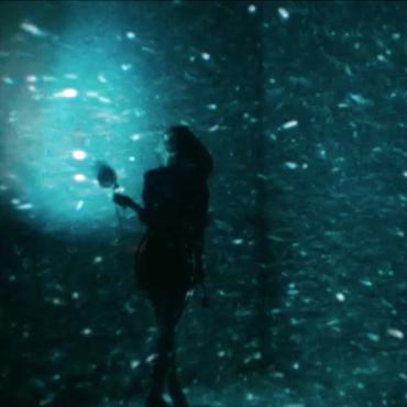 A woman in black facing towards a blue spotlight with flecks of white light all around.