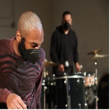 A dancer wearing a face mask in front of a drummer wearing a facemask.
