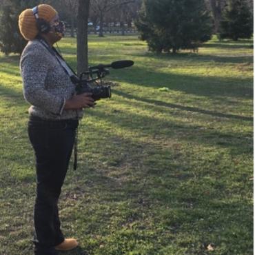 A filmmaker in the park, holding a camera.
