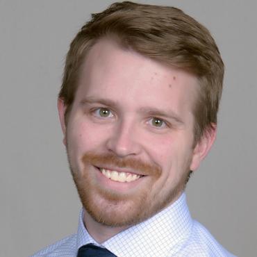 Kyle smiling at the camera wearing a shirt and tie