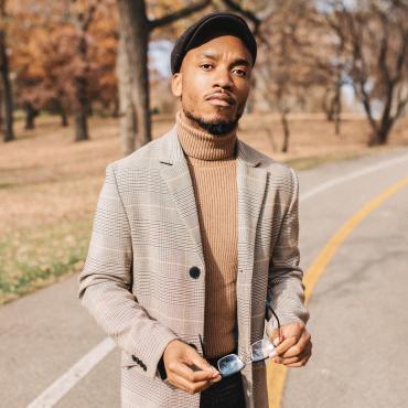 Donte Collins, a 26 year old Black poet, standing in the middle of a Bike Path in the fall among shedding aspen trees, holding their glasses.