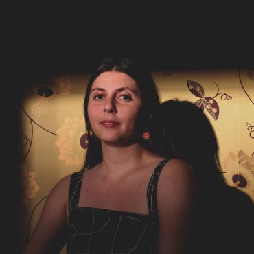 Amanda Ekery, a Syrian Mexican American musician in front of floral wallpaper