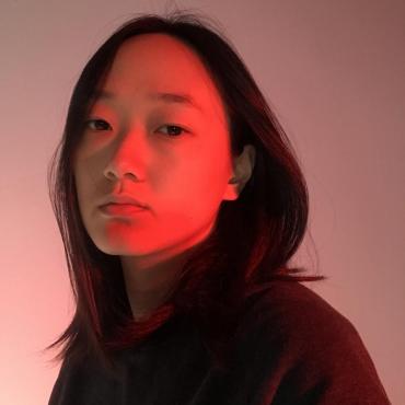 Shen Xin, a thirty-something asian person looking into the camera while being photographed under red studio light.