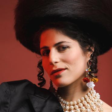 Lea Kalisch, a 28-year-old white woman wearing a Shtreimal (Jewish fur hat), a black coat over one shoulder and colorful jewelry.