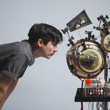 Efraín Rozas, looking at a robotic sculpture made up of percussion instruments and ornaments from different Peruvian cultures.
