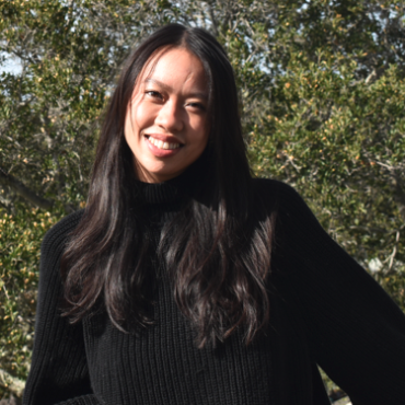 TA is smiling at the camera, outside with a large tree in the background.