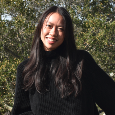 TA is smiling at the camera with a tree behind her