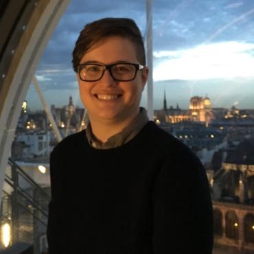 Andrea is smiling in front of a window with Paris in the background