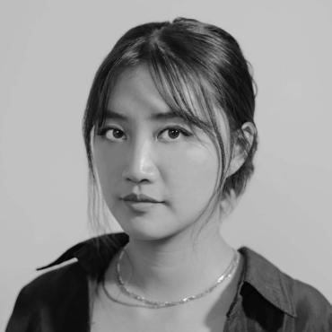 Black and white portrait of an Asian femme person looking into the camera.