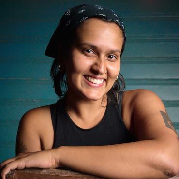 A headshot of filmmaker, Serena Hodges, they are smiling. They are wearing a black bandana and tank top.