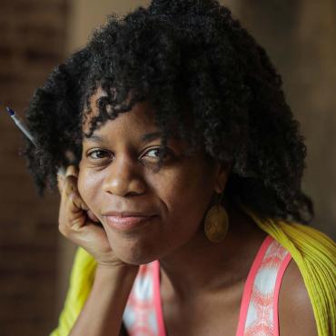 Headshot of Ama Codjoe, a black poet with shoulder-length natural hair, smiling.