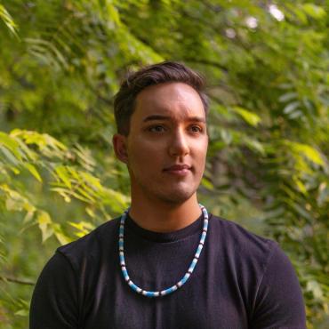 Headshot of Carson Faust, wearing a black shirt and a beaded blue, white, and black necklace by an Eastern Band Cherokee artist.