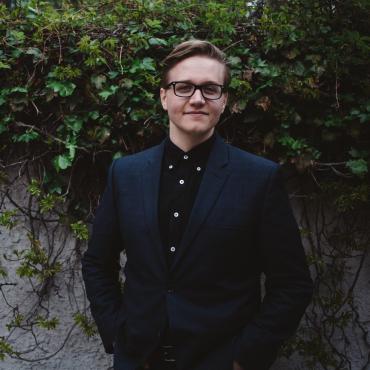 Billy Fidler, standing against a wall with foliage