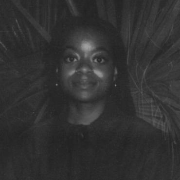 Crystal Kayiza, thirty-something Black woman, looking directing into camera