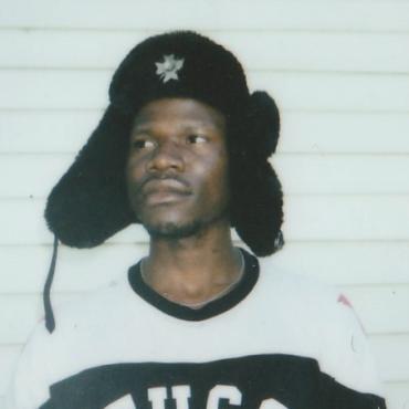 Olumide Famule, a late twenties Black man, with an Ushanka on looking away from the camera towards the sky.